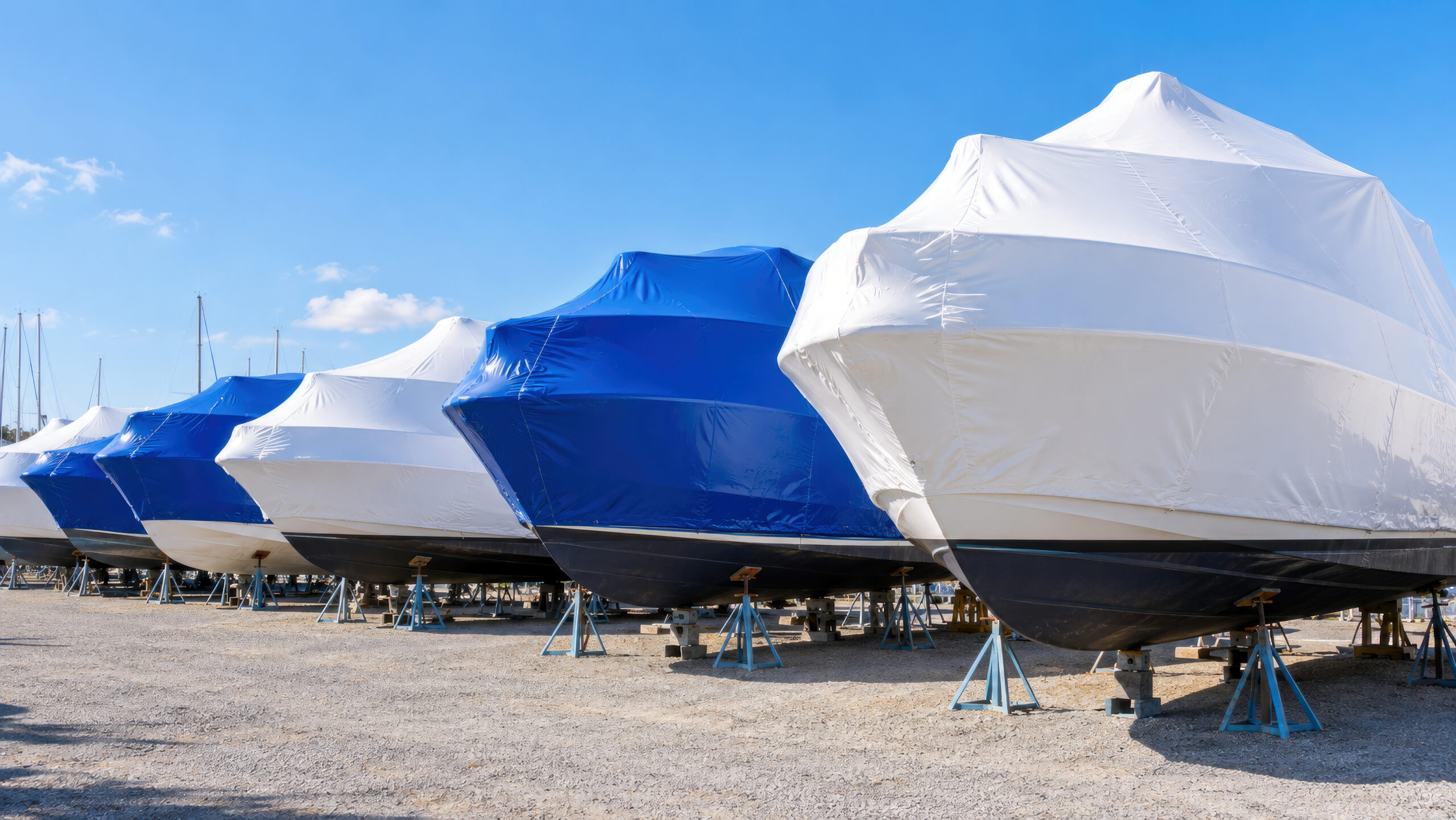 Row of boats in white and blue shrink wrap on stands in marina yard - winter boat storage